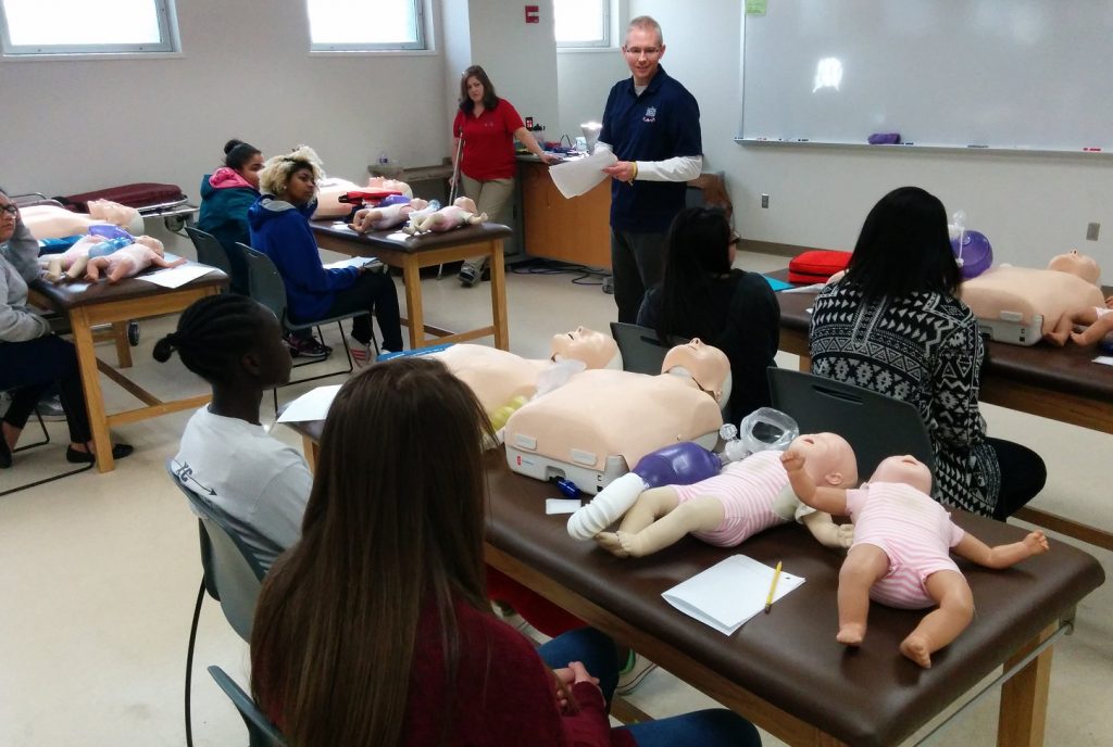 Instructor at front of classroom with CPR test dummies