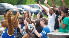 UMKC School of Education faculty, staff, students, and alumni with Kasey Kangaroo holding their hands up in celebration