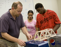 Mark Hieber, assistant teaching professor in the UMKC School of Computing and Engineering helps ARROWS participants test the strength of a popsicle stick bridge.