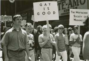 Activist Frank Kameny, surrounded by other protesters, smiles while holding a sign that reads "Gay is Good."