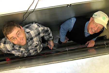 Brian Fricke and Bryan Becker installing meters and test devices behind a refrigeration unit.