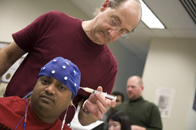 Jesse Sherwood, graduate research assistant and Ph.D. student, preps electrical engineering student Ramaraju Medisetty by injecting a conductive gel into the electrodes of the brain wave cap.